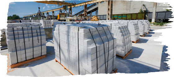 Dozens of pallets loaded with white aerated concrete blocks secured with straps, stored in an open industrial yard under a clear sky